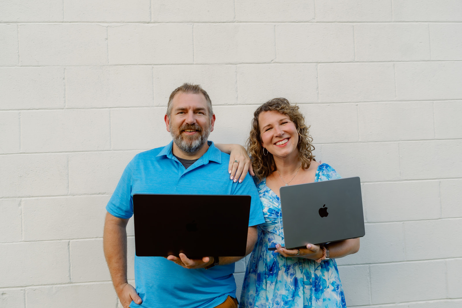 Anna and Bryan Cirlot holding open laptops against a white wall