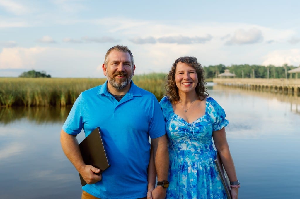 Anna and Bryan Cirlot, founders of Salt Marsh Digital, standing by a Gulf Coast marsh and boardwalk with laptops