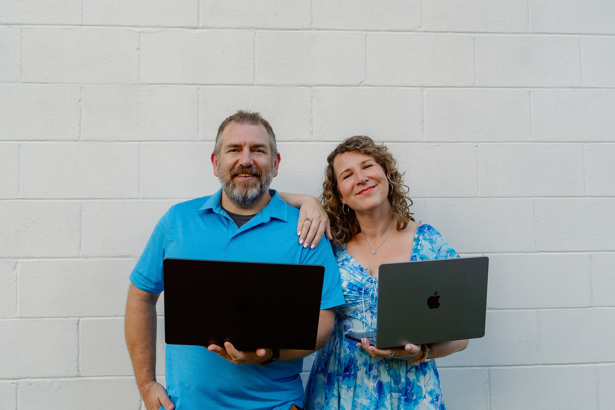 Anna and Bryan Cirlot holding laptops against a white wall, founders of Salt Marsh Digital