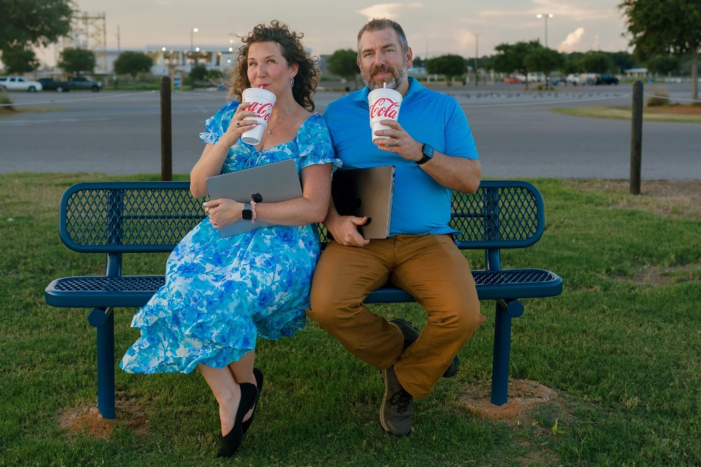 Salt Marsh Digital founders Anna and Bryan on a park bench with laptops, deadpan sipping large sodas